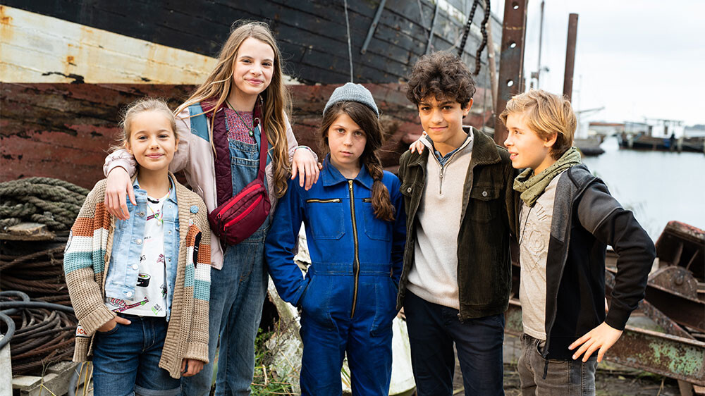 Szenenbild: Die fünf Pfefferkörner Clarissa, Alice, Hanna, Tarun und Johnny (von links nach rechts) stehen im Ostseehafen vor einem Schiff. Rechts im Hintergrund sieht man das Hafenbecken.