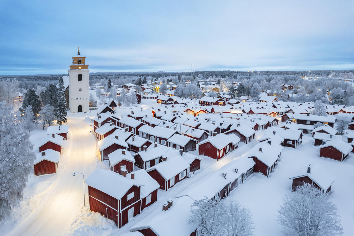 Gammelstad (auf Deutsch: Alte SWinterliche Luftaufnahme des alten, beleuchteten und schneebedeckten Gammelstad. Gammelstad (auf Deutsch: Alte Stadt) ist das historische Zentrum der Stadt Luleå. Das Dorf im Norden von Schweden gehört mit seiner Kirche und den roten Häusern zum UNESCO-Welterbe.