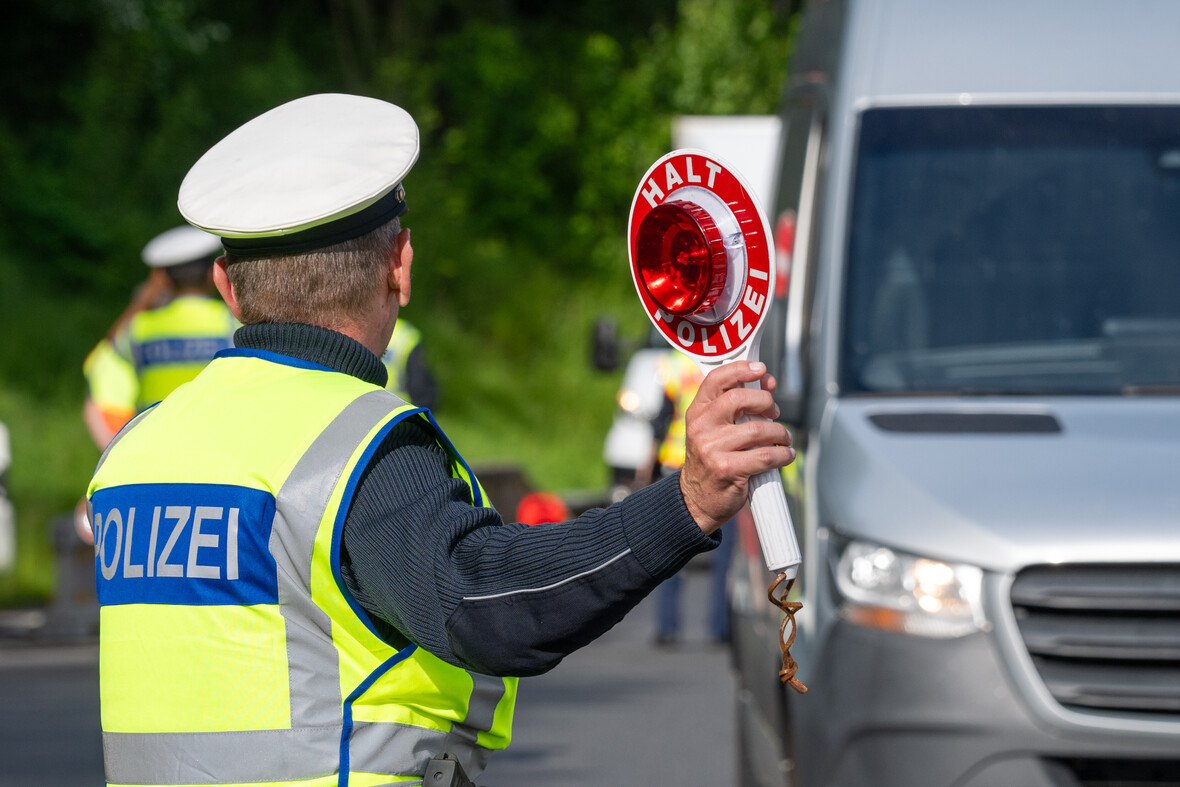 Ein Polizist winkt einen grauen Transporter zu einer Verkehrskontrolle raus. 
