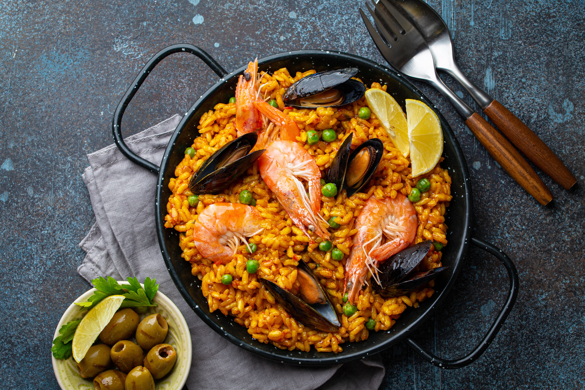 Spanische Paella mit Garnelen, Garnelen, Muscheln, grünen Erbsen und frischen Zitronenschnitzen von oben. Paella ist klassisches Gericht aus Spanien.