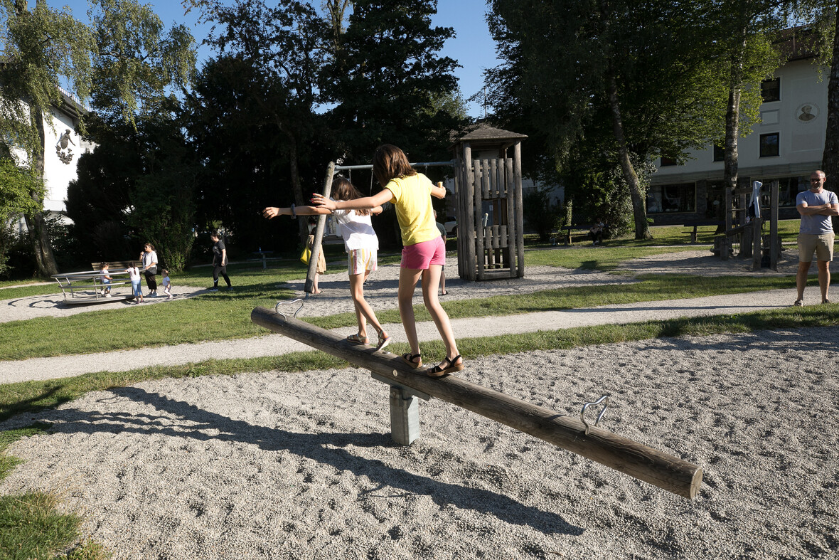 Zwei Kinder balancieren auf einem Holzstamm auf einem Spielplatz.