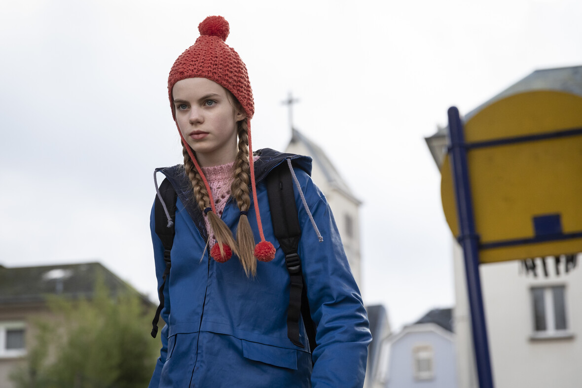 Ulja läuft mit blauer Regenjacke und roter Mütze durch die Straßen. 