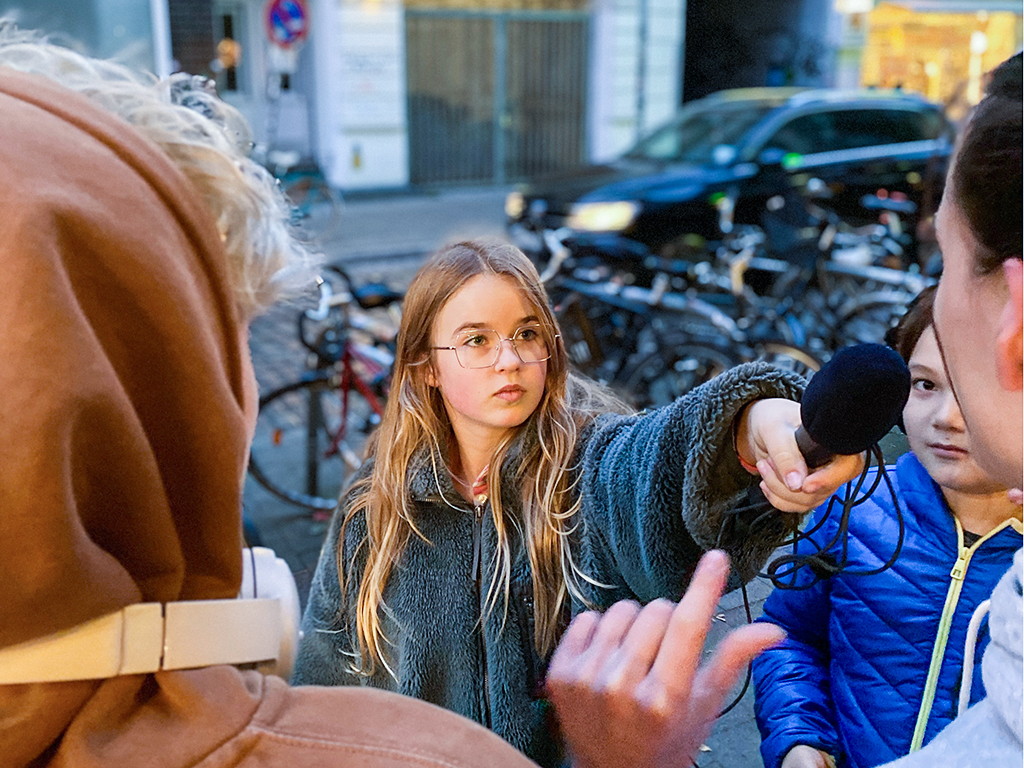 Man sieht ein Mädchen, was gerade jemanden interviewt und ein Mikrofon hält.